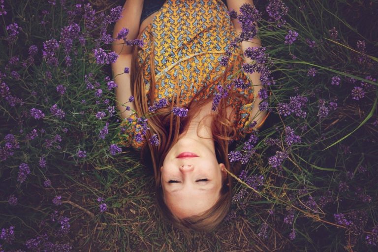 Una mujer tumbada en sobre cesped, se encuentra tranquila y relajada rodeada de flores moradas